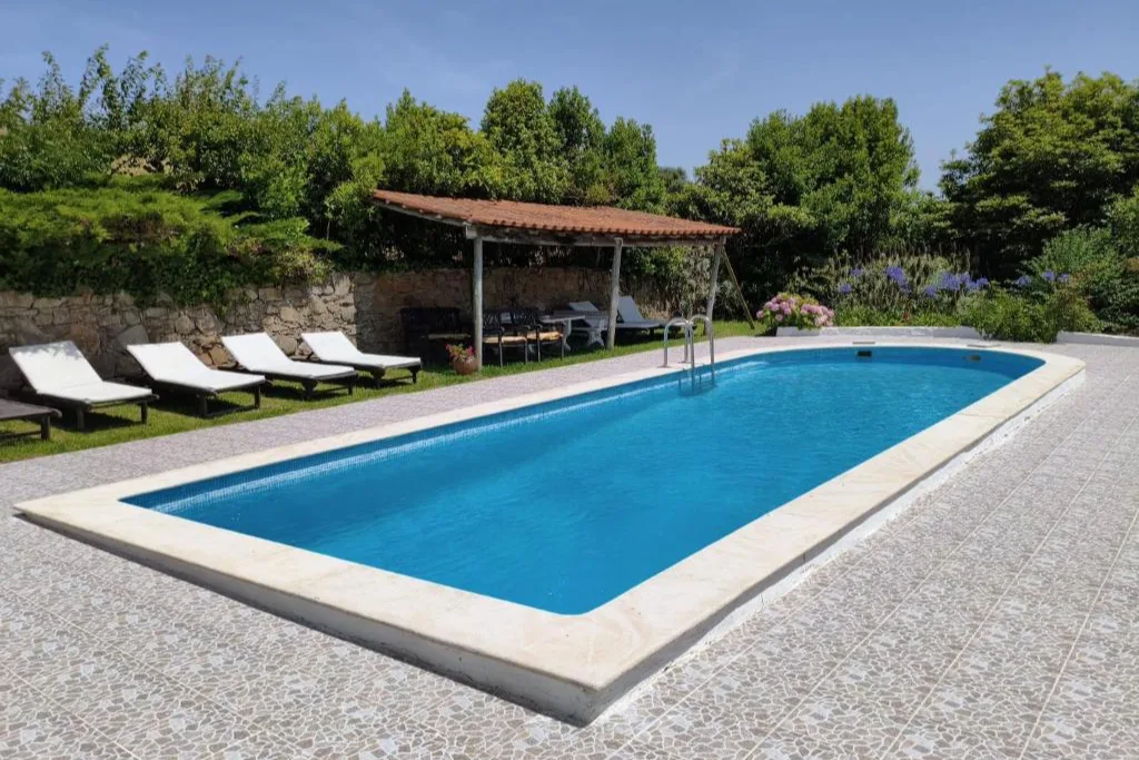 A piscina exterior, com as espreguiçadeiras e o alpendre com sombra